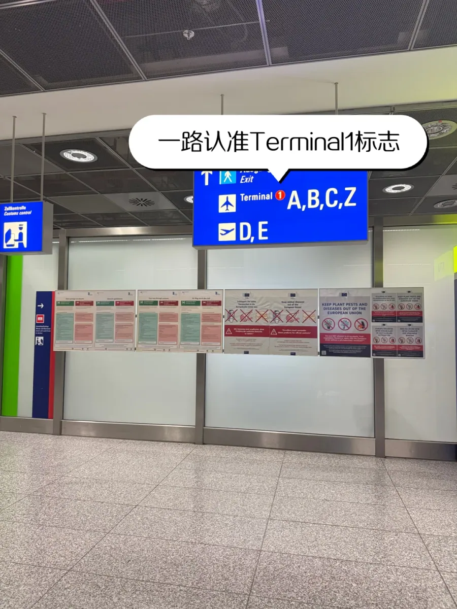 Blue sign in a Terminal 2 arrivals corridor, reading "Terminal 1 A,B,C,Z" above "D,E"