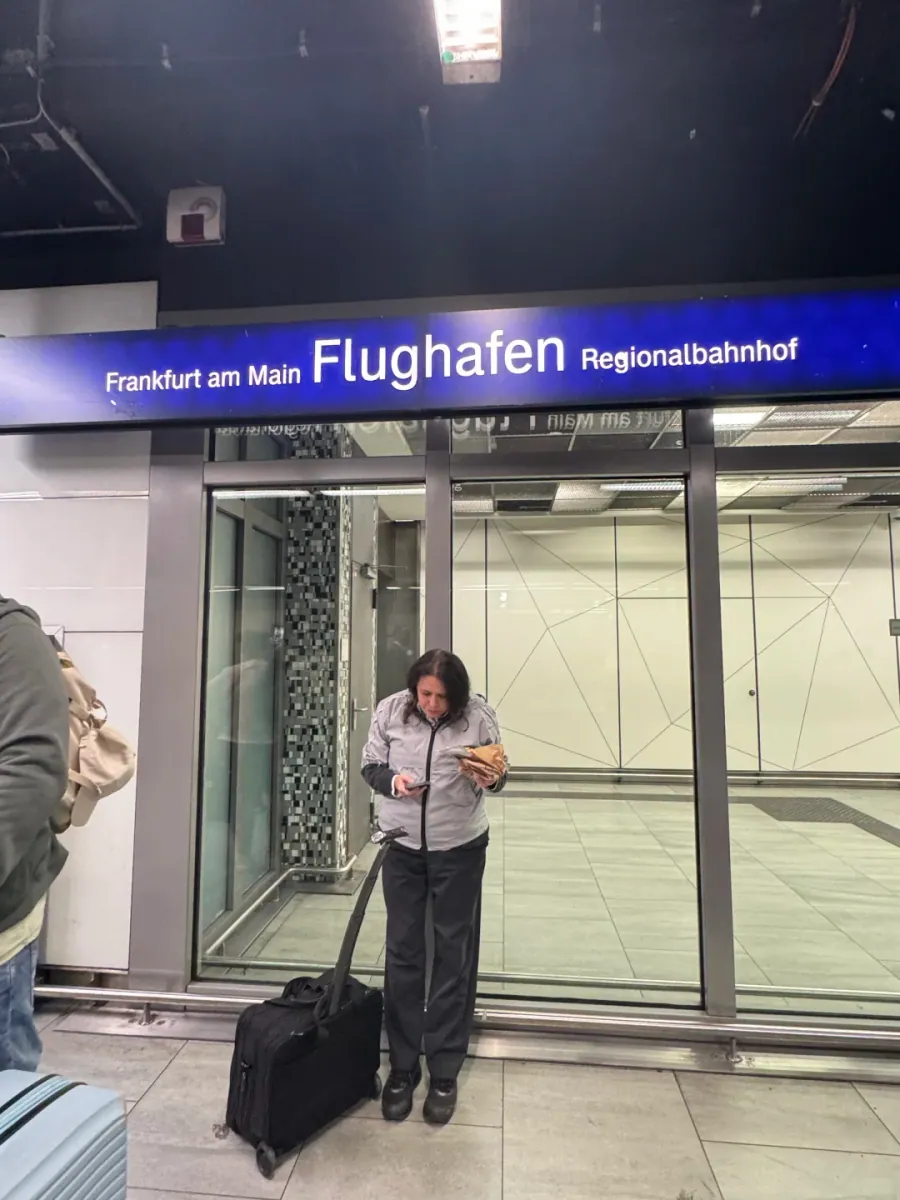 The regional station platform: a blue sign reading Frankfurt am Main Flughafen Regionalbahnhof, with a traveller and a suitcase standing by the glass doors