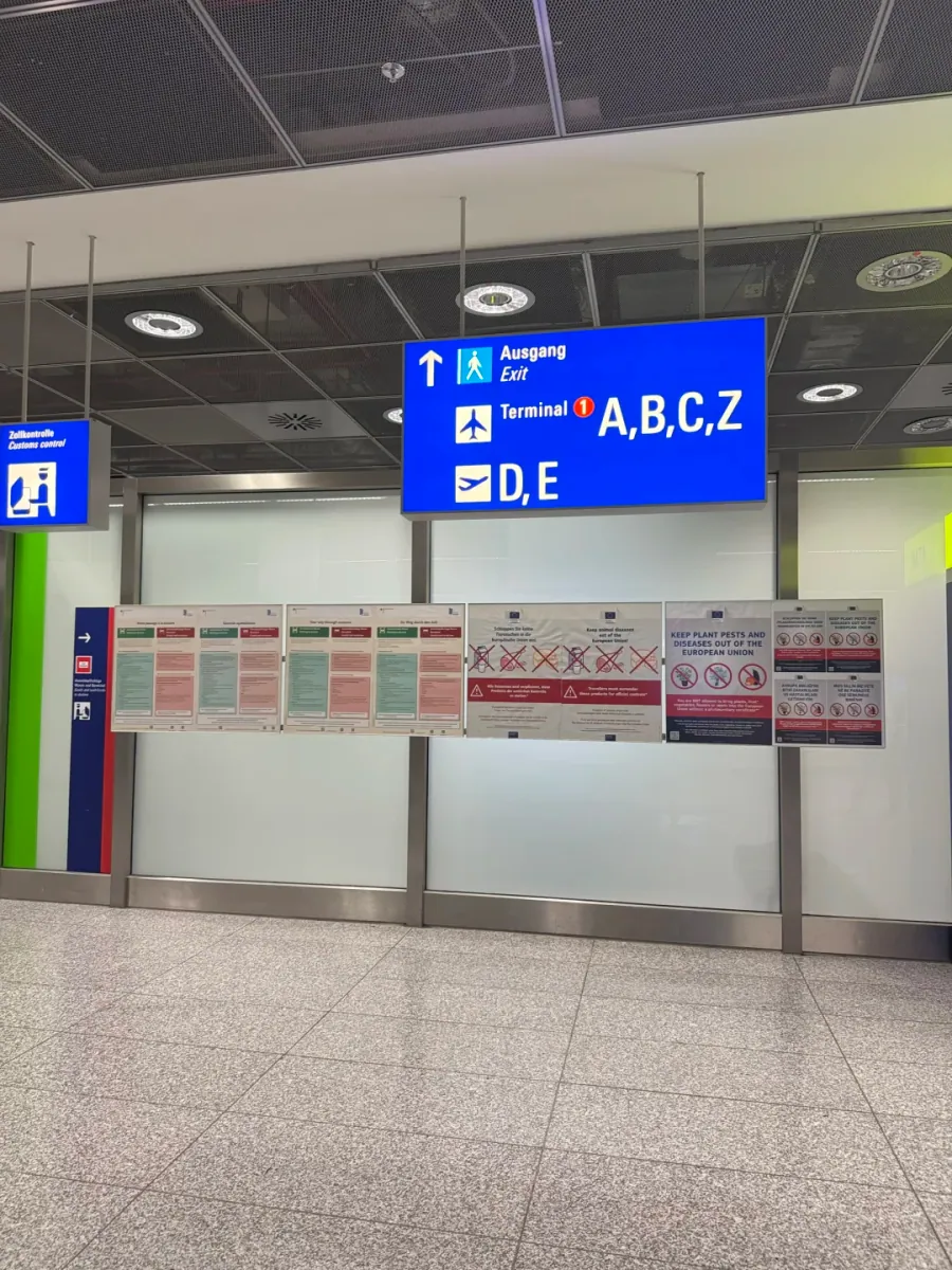 Close-up of a Terminal 2 sign: Ausgang/Exit above "Terminal 1 A,B,C,Z" and "D,E", with quarantine notices on the wall behind