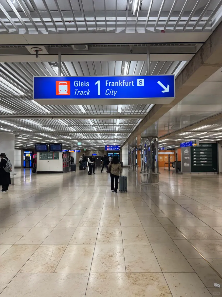 A blue sign in the regional station concourse: Gleis 1/Track 1 towards Frankfurt City, with the S-Bahn logo and a diagonal down arrow