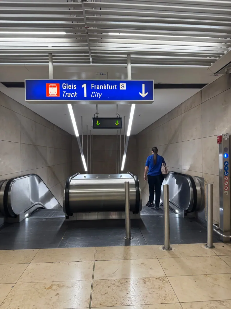 An escalator down to the S-Bahn platforms, with a sign overhead reading Gleis 1/Track 1 and Frankfurt