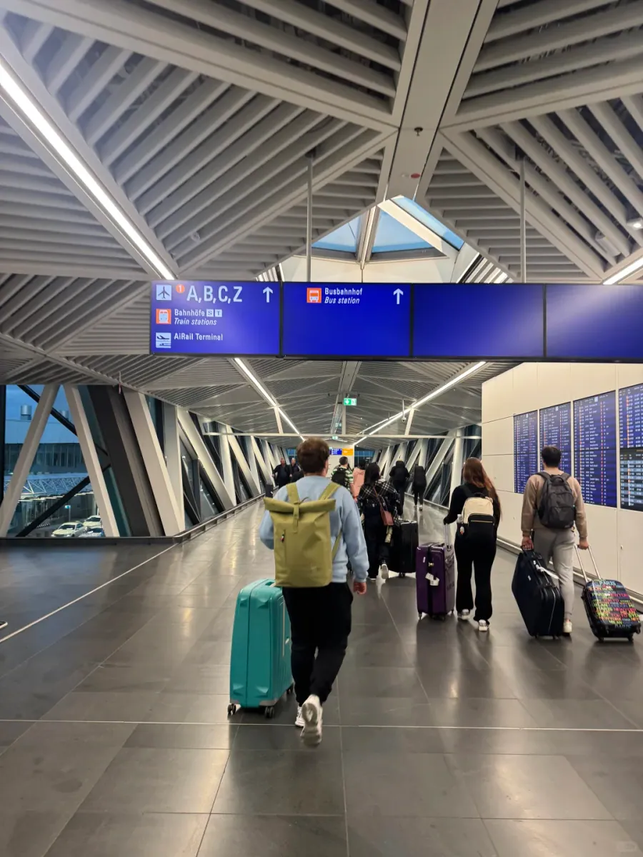 A corridor in Terminal 3 towards the SkyLine: blue signs reading "A,B,C,Z", Bahnhöfe/Train stations and Busbahnhof, with travellers pulling cases