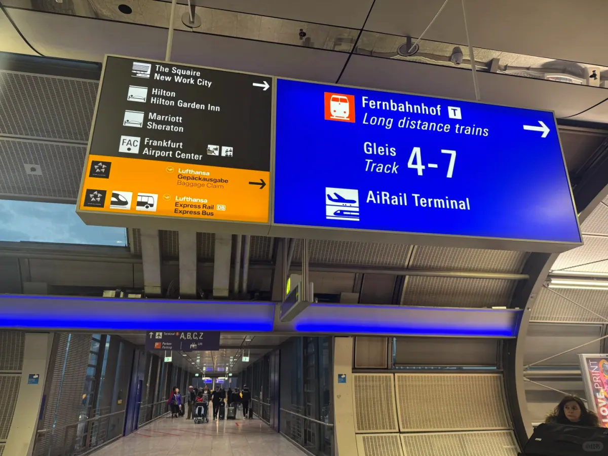 A blue sign above a station entrance in Terminal 1: Fernbahnhof/Long distance trains, Gleis 4–7 and AiRail Terminal, with an arrow pointing to the corridor