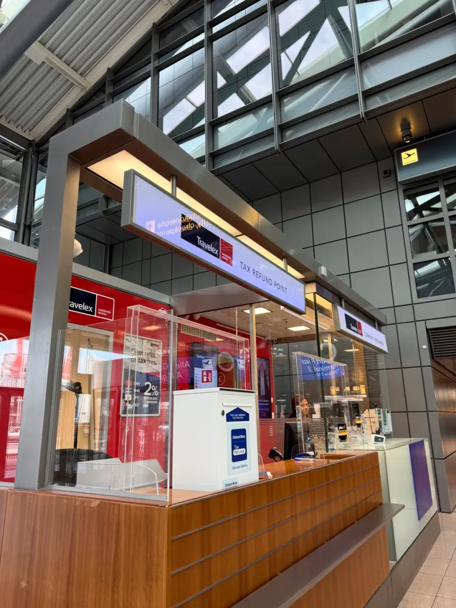 The Travelex TAX REFUND POINT counter at Hamburg Airport: red walls and a wooden desk, staff behind a glass screen, and a white Global Blue drop box on the counter