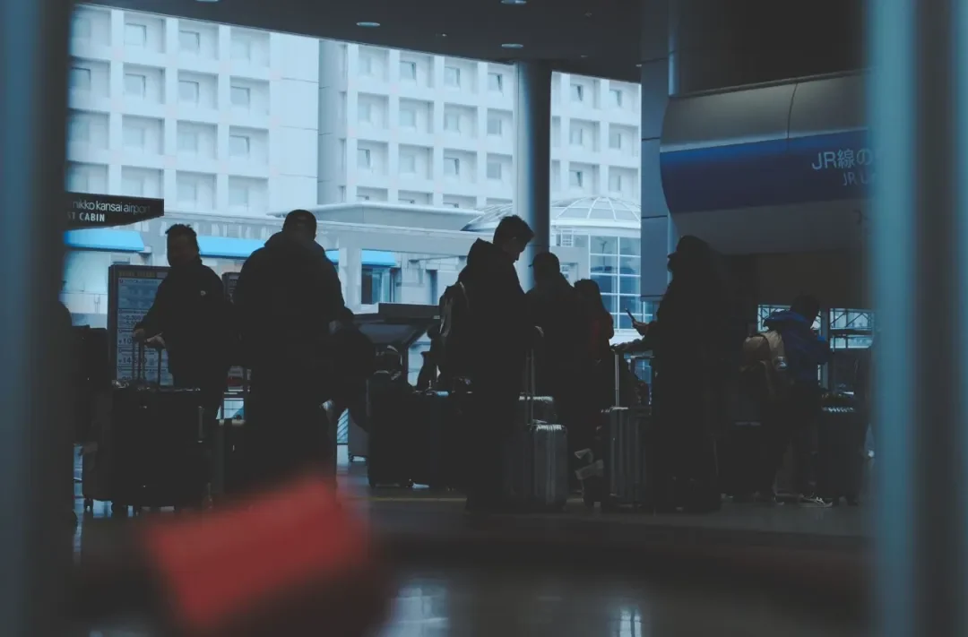 Passengers with luggage on the arrivals floor at Kansai Airport, with JR line signage on the right