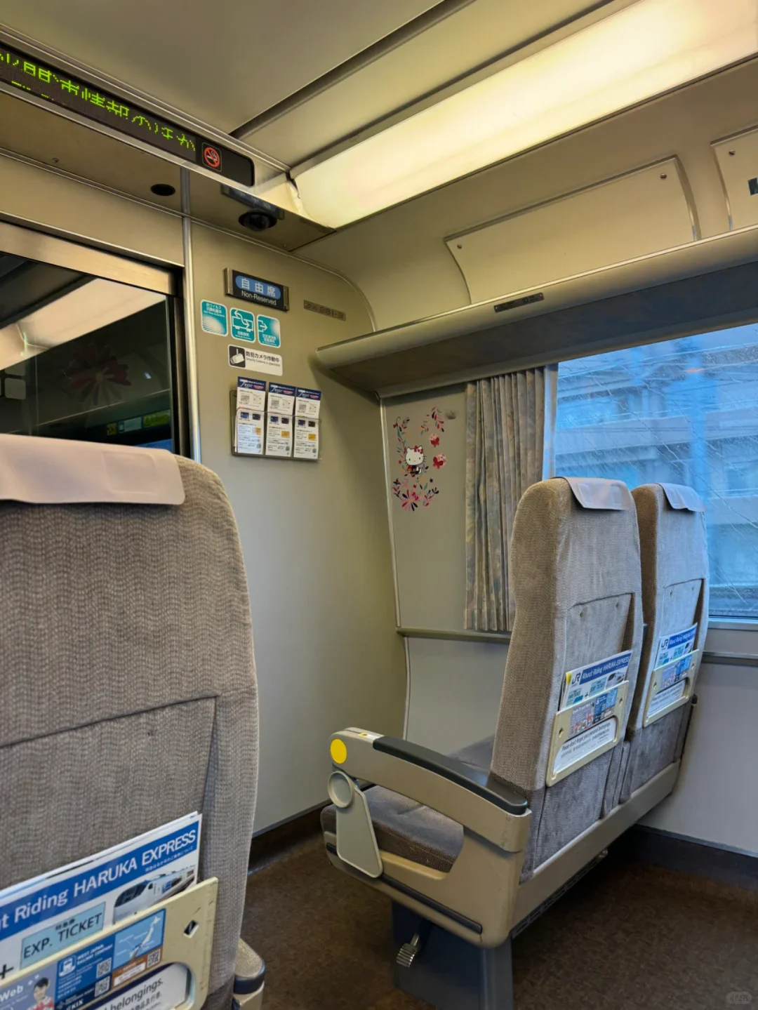 Inside a non-reserved HARUKA car: grey-beige seats and luggage space by the windows
