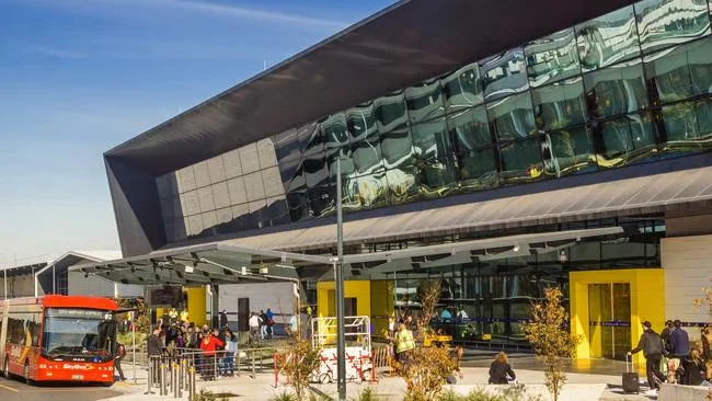 The kerbside drop-off area outside a Melbourne Airport terminal, with a red airport bus at the kerb
