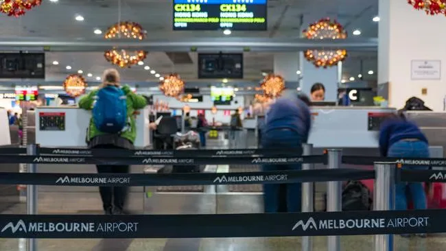 A check-in and bag-drop area at Melbourne Airport, with queue barriers carrying the airport logo
