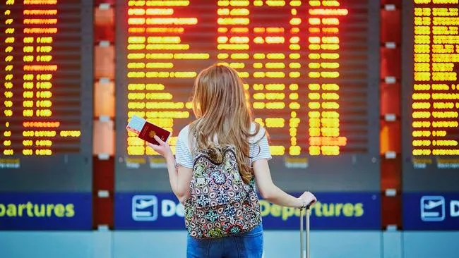 A passenger with a passport and backpack reading the departures board at Melbourne Airport