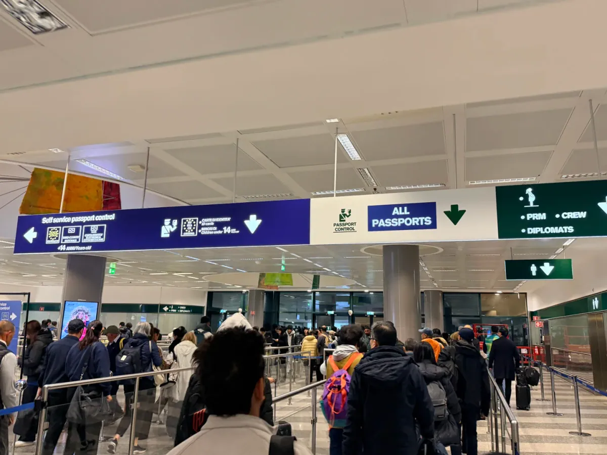 A junction sign: an arrow left to Self service passport control, the ID card and under-14 lane in the middle, a blue ALL PASSPORTS arrow pointing down on the right and a green sign for PRM, CREW and DIPLOMATS