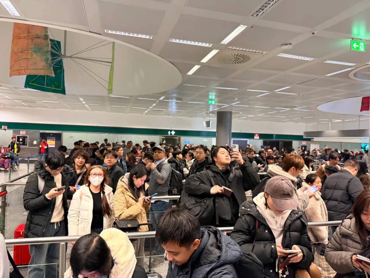The queue itself: passengers in winter coats looking at their phones, suitcases parked against the barriers, the line stretching out of sight