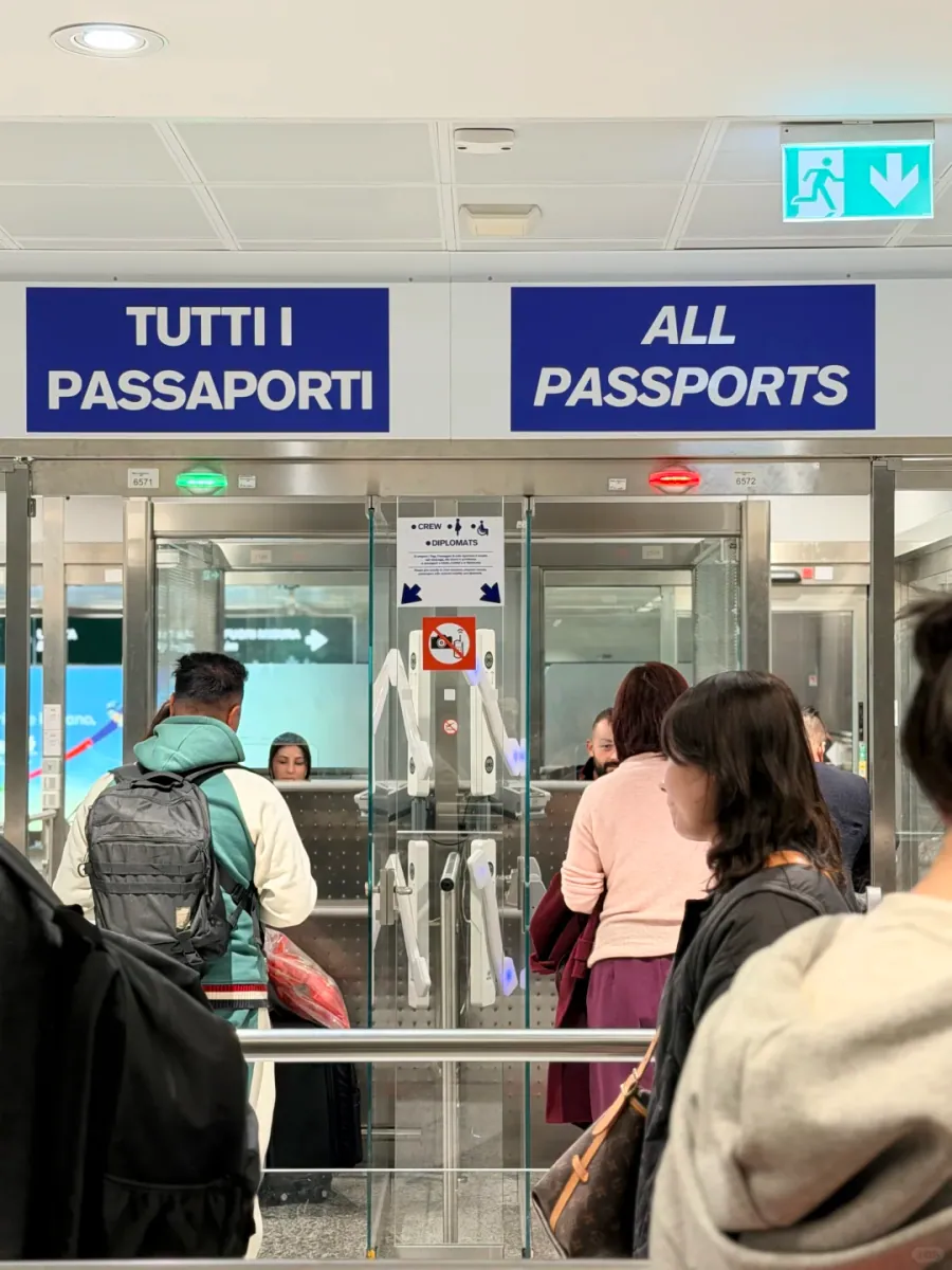 Glass booths and a manual desk beneath a blue TUTTI I PASSAPORTI / ALL PASSPORTS sign, with passengers at the counter