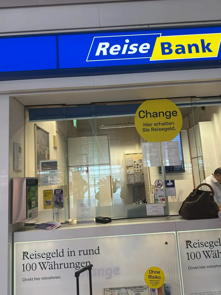 The Reise Bank counter at Munich Airport: a blue and yellow sign, a yellow Change roundel on the glass, and a poster reading "Reisegeld in rund 100 Währungen"