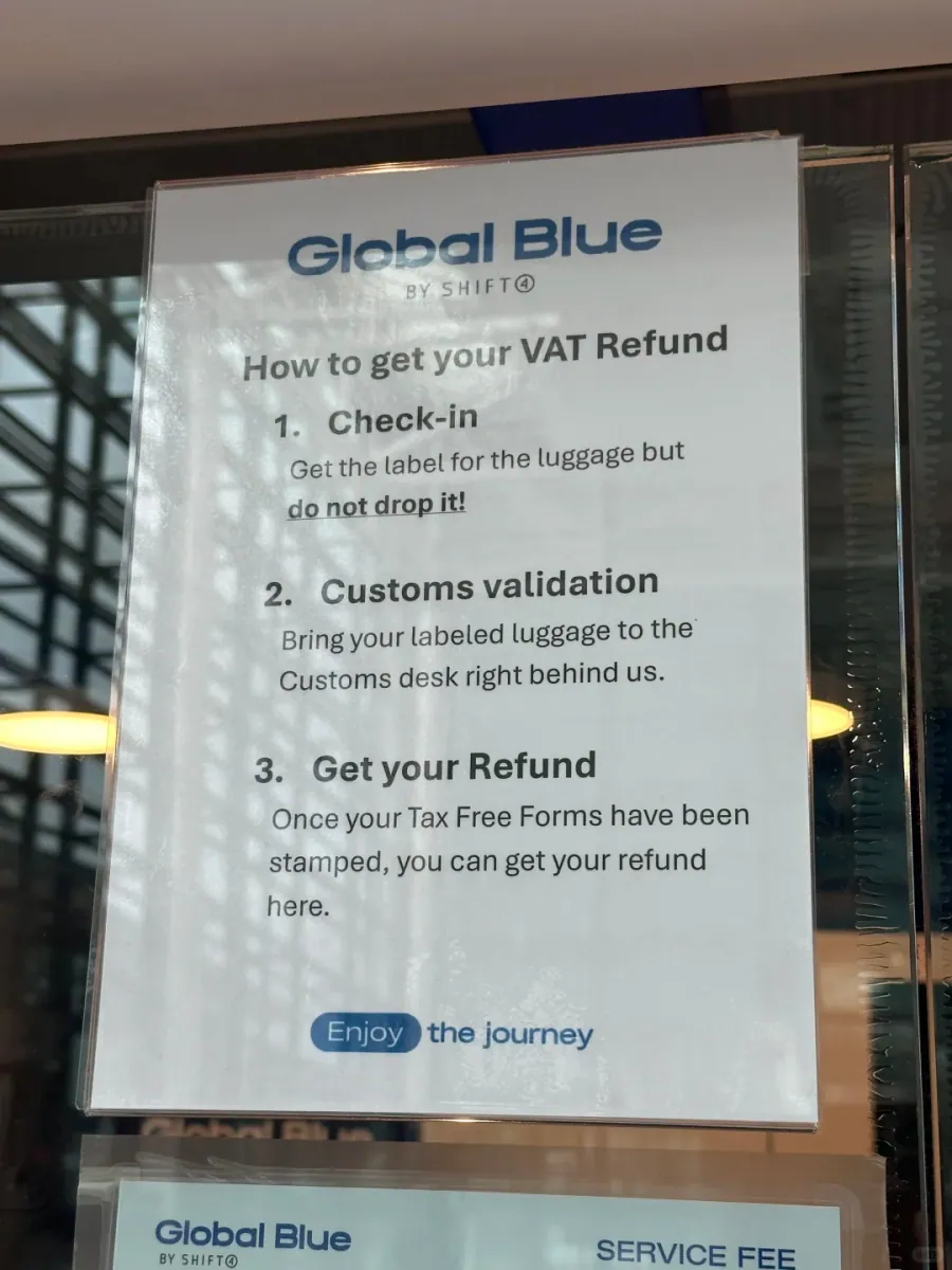 A Global Blue notice on the counter headed "How to get your VAT Refund", listing check-in, customs validation and the refund, and warning not to drop the labelled luggage