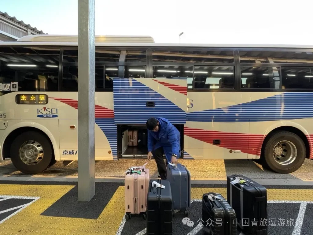 Staff loading suitcases into the coach's luggage hold, with bags queued on the stand