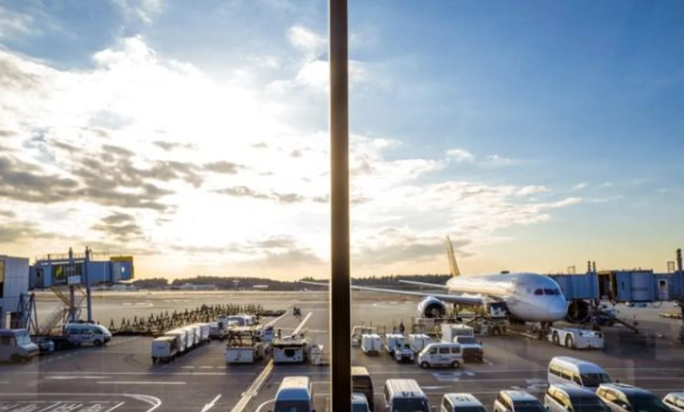The apron seen from a Narita Airport observation deck, with an aircraft and ground vehicles in the evening light
