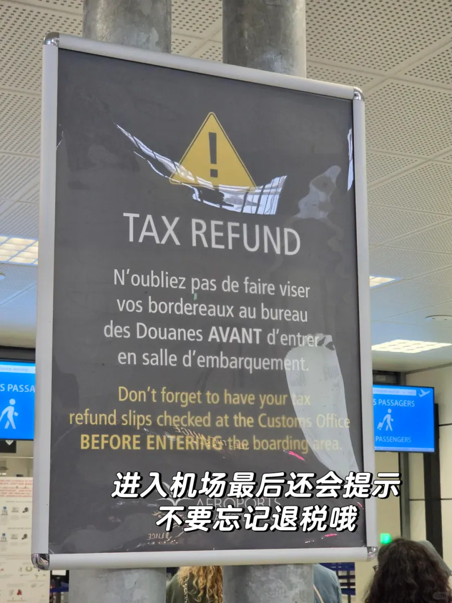 A dark grey TAX REFUND notice board in an airport corridor: under a yellow warning triangle, French and English text reminds travellers to have their refund slips checked at the customs office before entering the boarding area