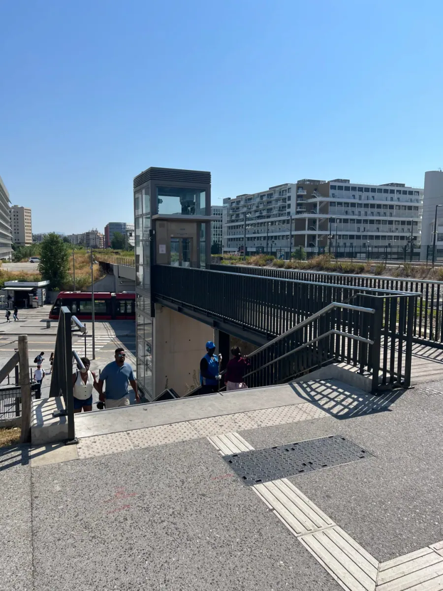 The steps beside the footbridge and the glass lift tower, with apartment blocks and the railway embankment behind