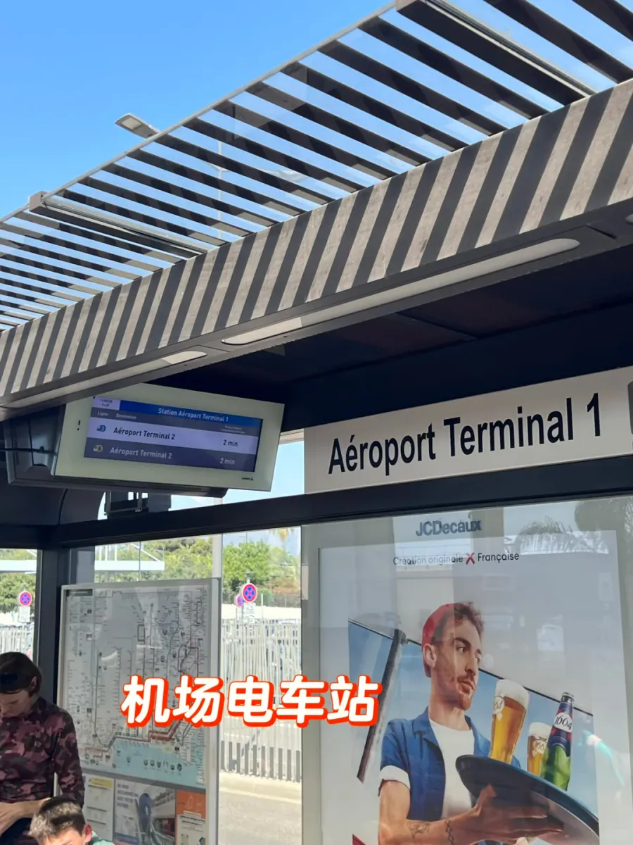 The "Aéroport Terminal 1" tram stop: a slatted canopy, a display showing the next Terminal 2 service in two minutes, and a shelter below