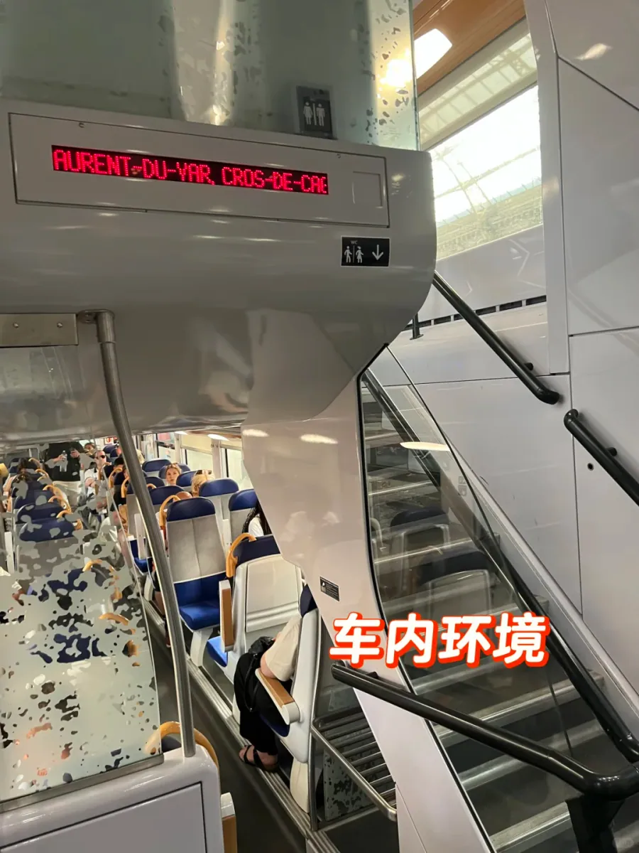Inside a TER carriage: the staircase of a double-decker, blue seats and a red LED sign scrolling the destination towards Cagnes