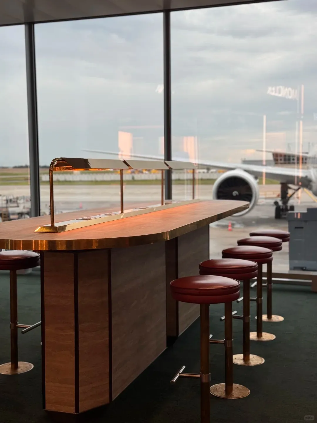 A long bar counter and bar stools facing the window in a Paris CDG departure area, with an aircraft engine visible outside