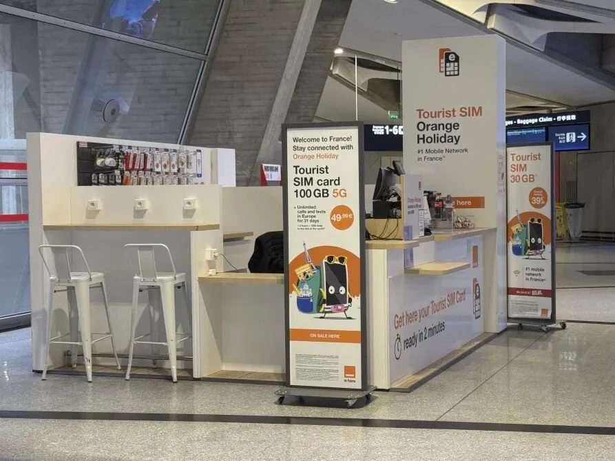 The Orange tourist SIM counter at Paris CDG, advertising "Tourist SIM card 100GB 5G" at €49.99 and ready in 2 minutes