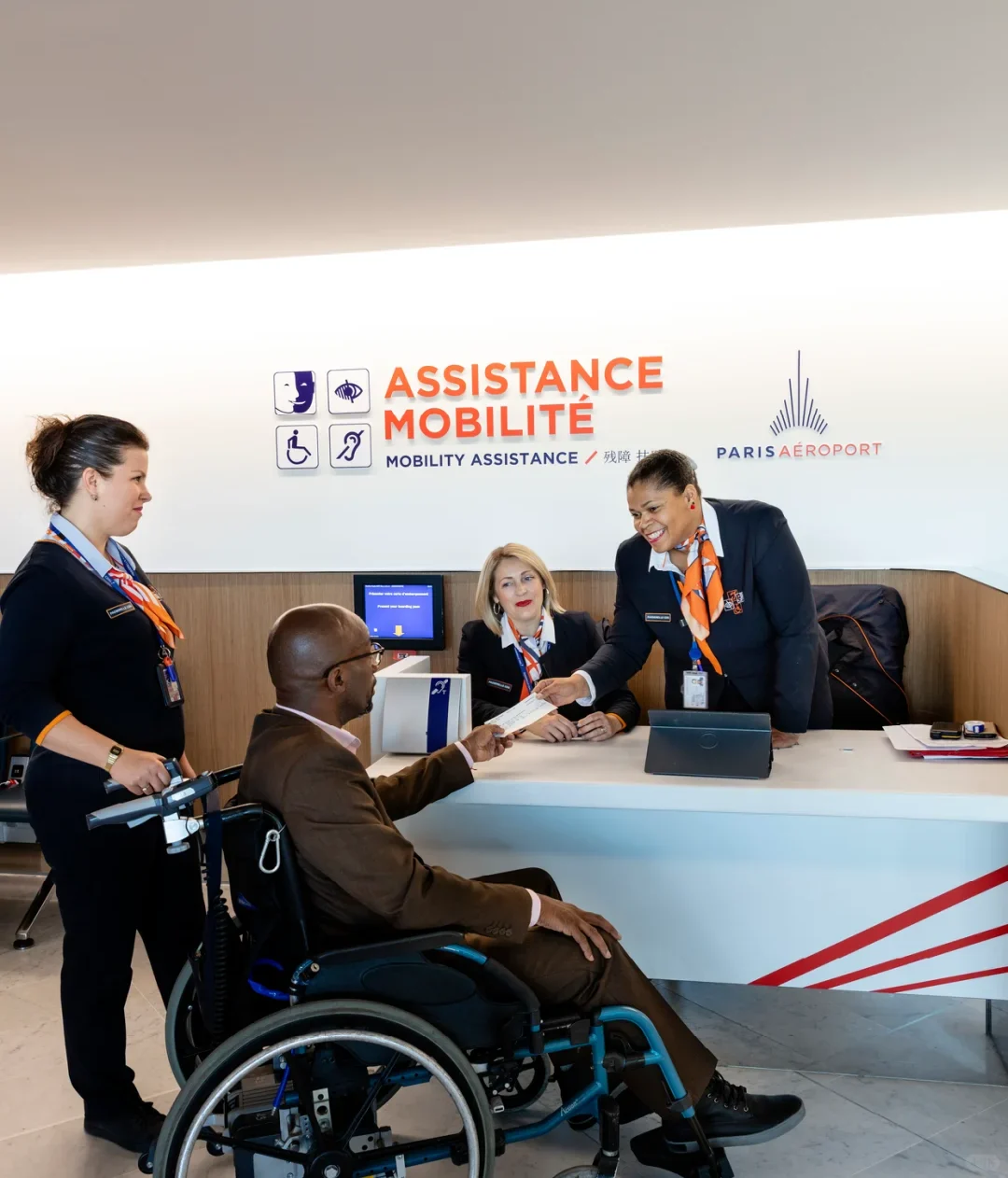 The Paris Aéroport "ASSISTANCE MOBILITÉ / MOBILITY ASSISTANCE" desk, with staff helping a passenger in a wheelchair