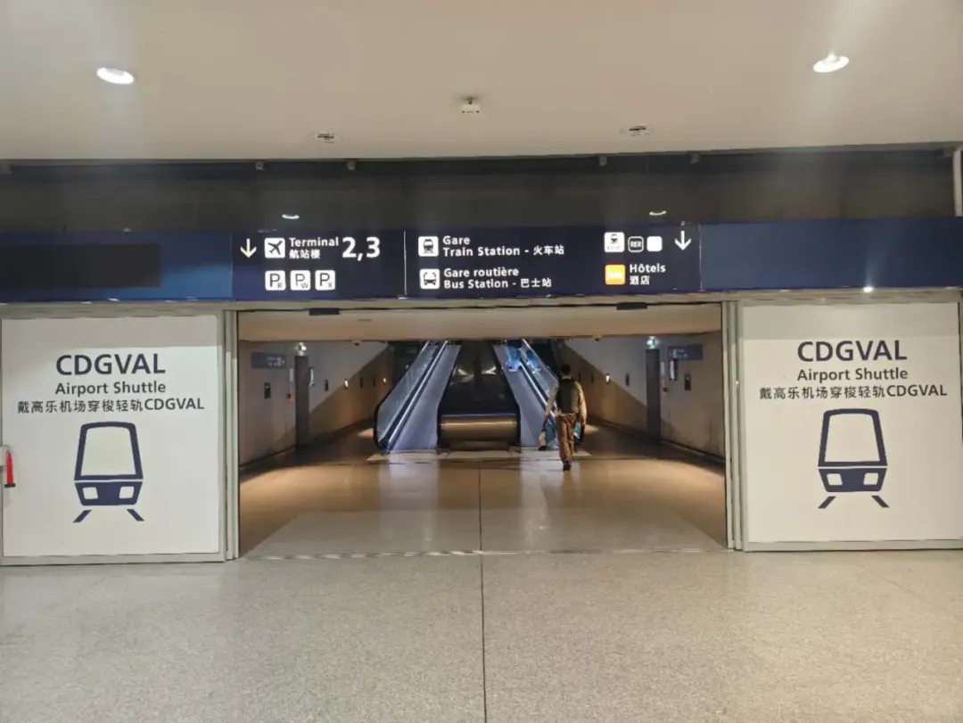 The CDGVAL entrance at Paris CDG, signed "CDGVAL Airport Shuttle 戴高乐机场穿梭轻轨", with directions overhead to Terminals 2 and 3, the railway station and the bus station