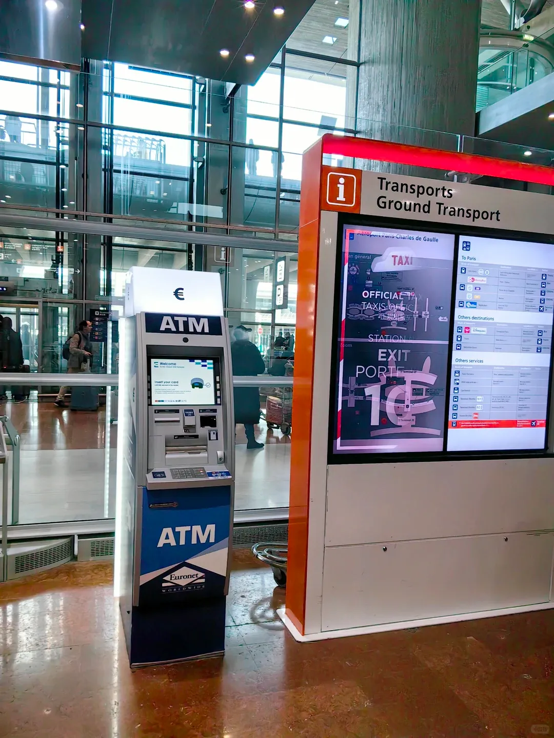 An ATM in the CDG arrivals area, beside a "Transports / Ground Transport" information pillar