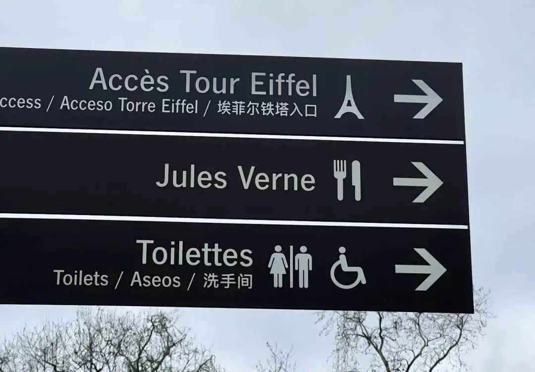 A Paris sign carrying Chinese: Accès Tour Eiffel / 埃菲尔铁塔入口 and Toilettes / Toilets / 洗手间