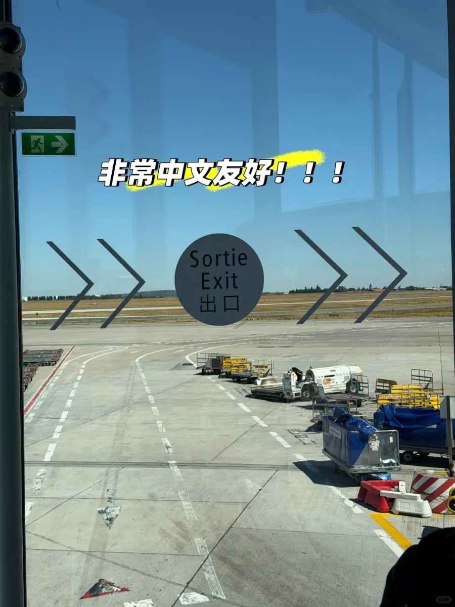 A round "Sortie / Exit / 出口" sticker with four arrows on the jet-bridge glass, the apron and baggage carts outside, and a green exit sign at upper left
