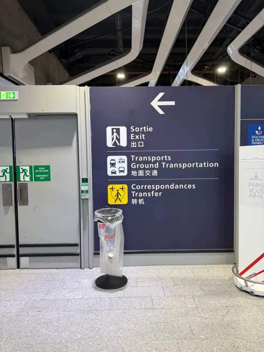 A dark blue sign wall: a left arrow above Sortie / Exit / 出口, Transports / Ground Transportation / 地面交通 and Correspondances / Transfer / 转机
