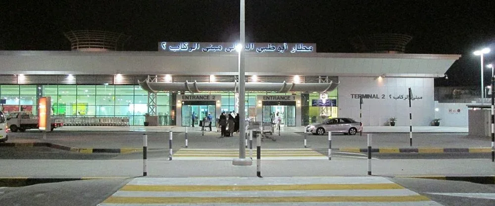 Terminal 2 des Al Ain International Airport bei Nacht, die Eingänge beleuchtet unter der arabischen Beschriftung von Abu Dhabi Airports.