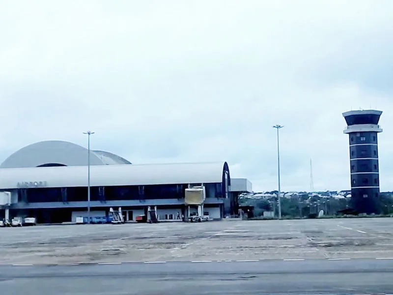 Das Terminal vom Vorfeld aus: weiße Gewölbedächer neben dem freistehenden Kontrollturm, unter Reihen von Flutlichtmasten.