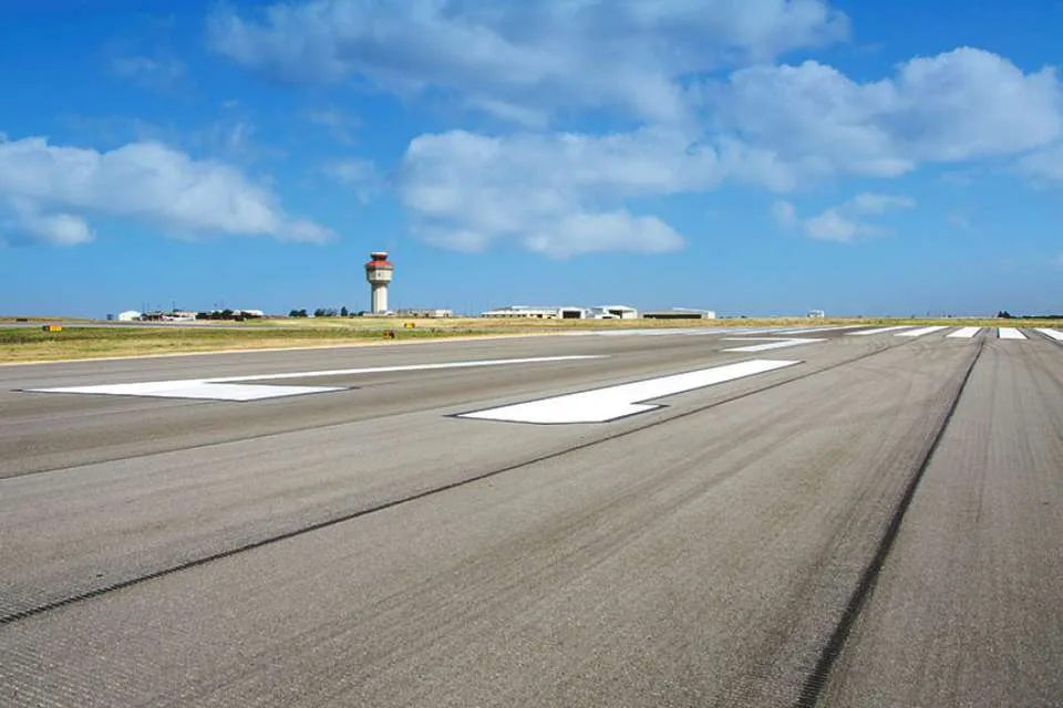 Blick die Startbahn entlang zum Tower – weiße Markierungen ziehen sich über den dunklen Asphalt bis zum rot-weißen Tower am Horizont.