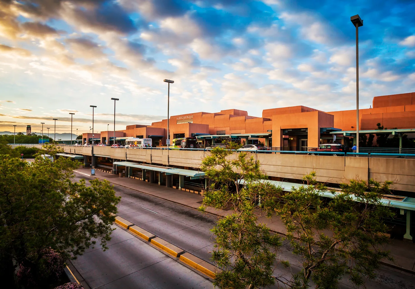Die Landseite des Terminals — „ALBUQUERQUE“ leuchtet auf den Terrakotta-Blöcken im Pueblo-Revival-Stil, unten auf der Straße Shuttles und Autos.