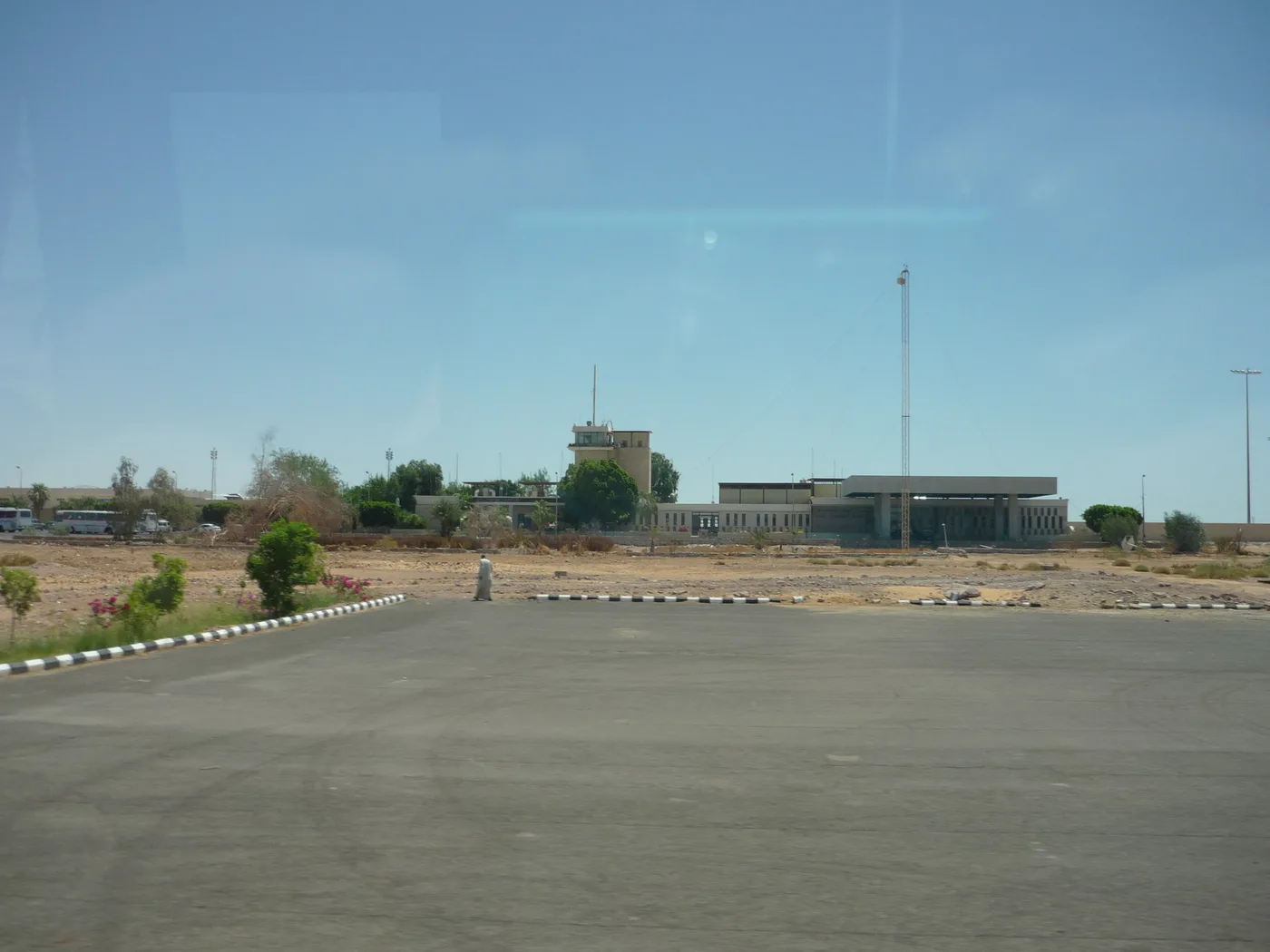 Der Flughafen von seiner Zufahrtsstraße: ein niedriges Terminal und ein Turm zwischen Bäumen, ringsum Wüste.