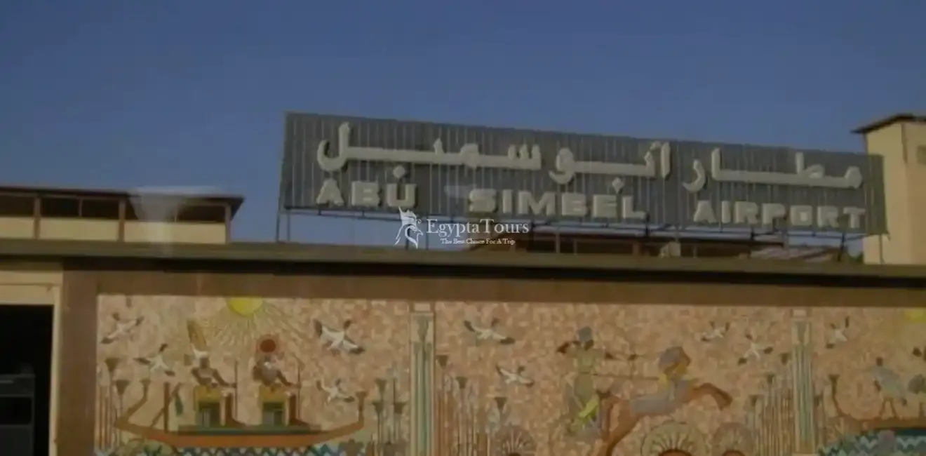 Das Schild „ABU SIMBEL AIRPORT“ auf dem Terminaldach, über einer Wand mit Wandbildern im Stil des alten Ägypten.
