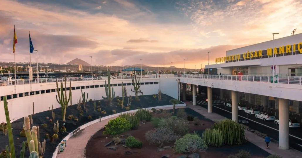 César Manrique-Lanzarote Airport in der Dämmerung — das Schild des Flughafens über einem versenkten Kakteengarten, dahinter die Hügel der Insel.