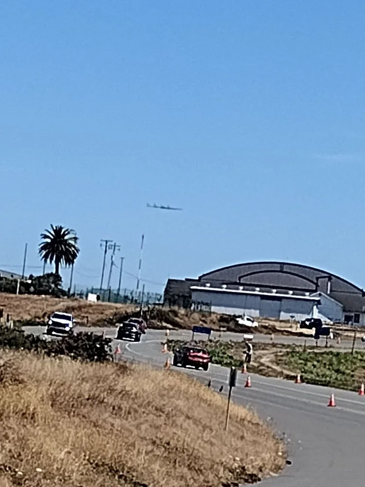 Neben dem Flugfeld: Verkehr fährt an den Hangars vorbei, während ein leichtes Propellerflugzeug über der Startbahn steigt.