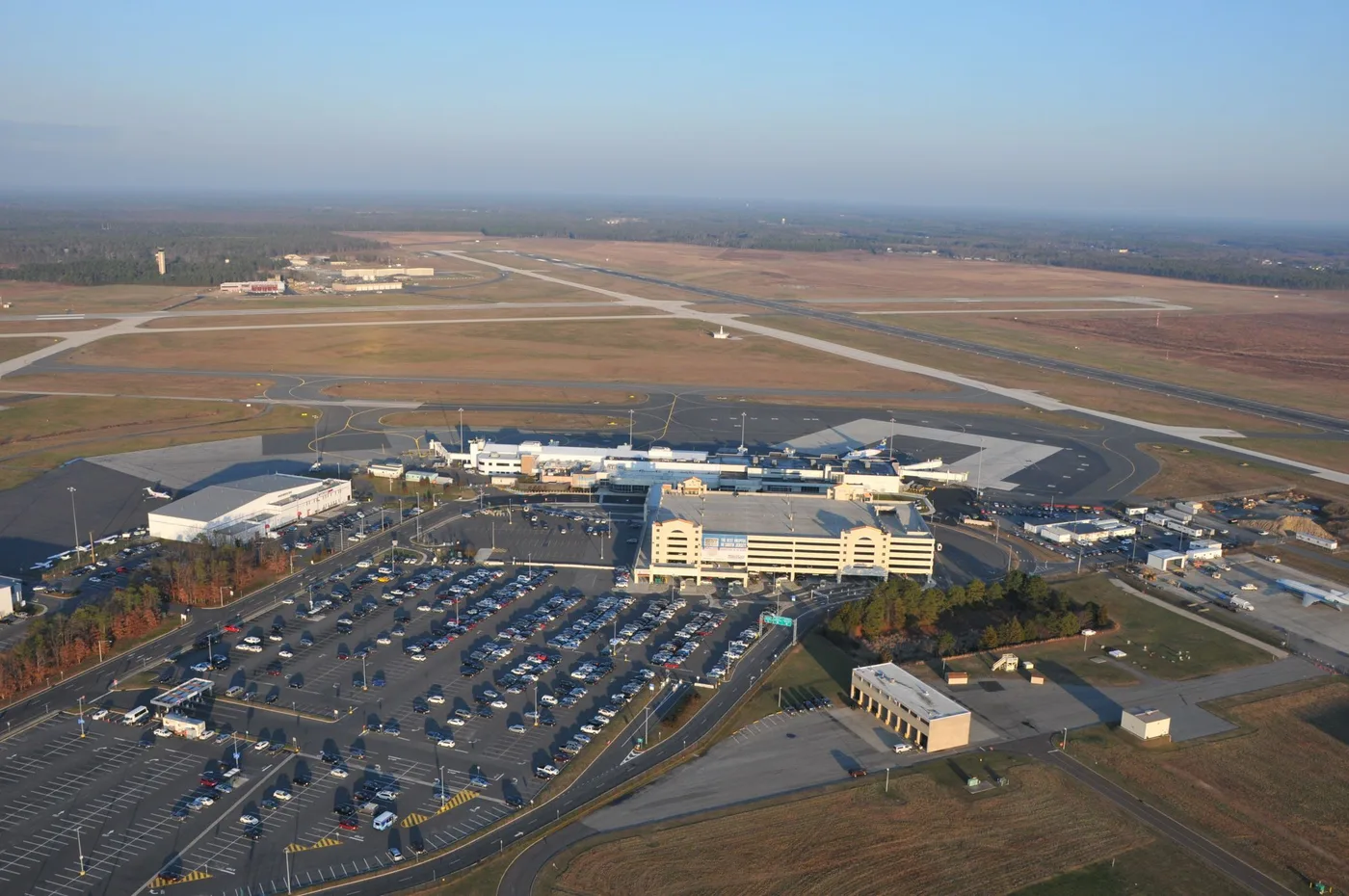Luftaufnahme von Atlantic City International: Terminal und Wartehalle in der Mitte, ringsum Parkplätze und Rollwege, am Horizont die Skyline der Stadt.