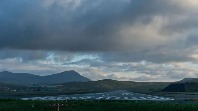 Adak am Ende der Startbahn – tiefe Bewölkung über den Vulkanhügeln, die beleuchtete Startbahn zieht sich zu deren Fuß.