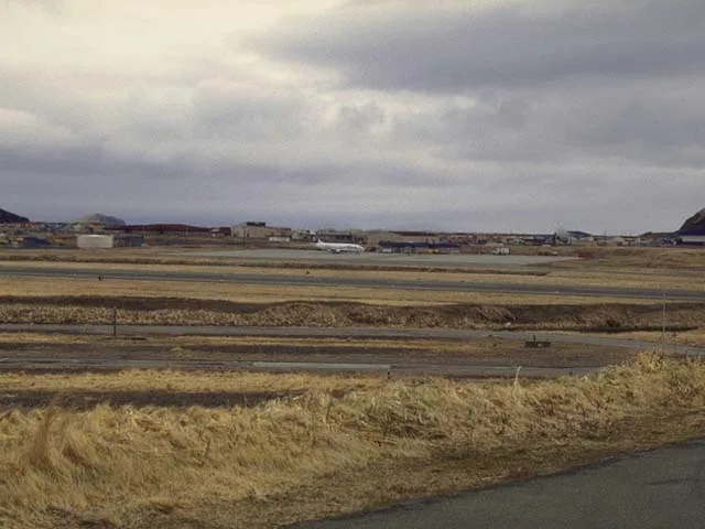 Über die Tundra zum Flugfeld von Adak – Start- und Rollbahn liegen flach im Gelände, die Flughafengebäude klein am Horizont.