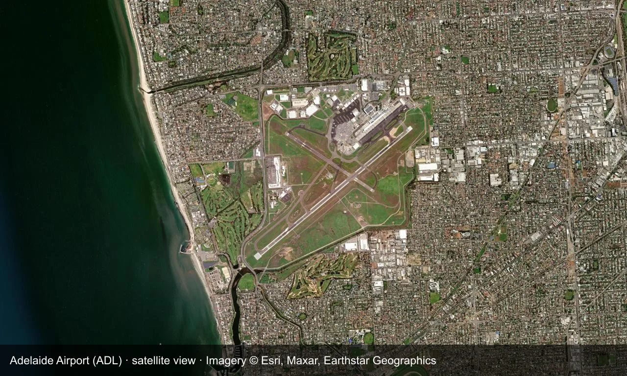Satellitenansicht: Startbahn und Terminal von Adelaide liegen westlich des Stadtzentrums, mit Hafen, Industrie und Wohnbebauung ringsum.
