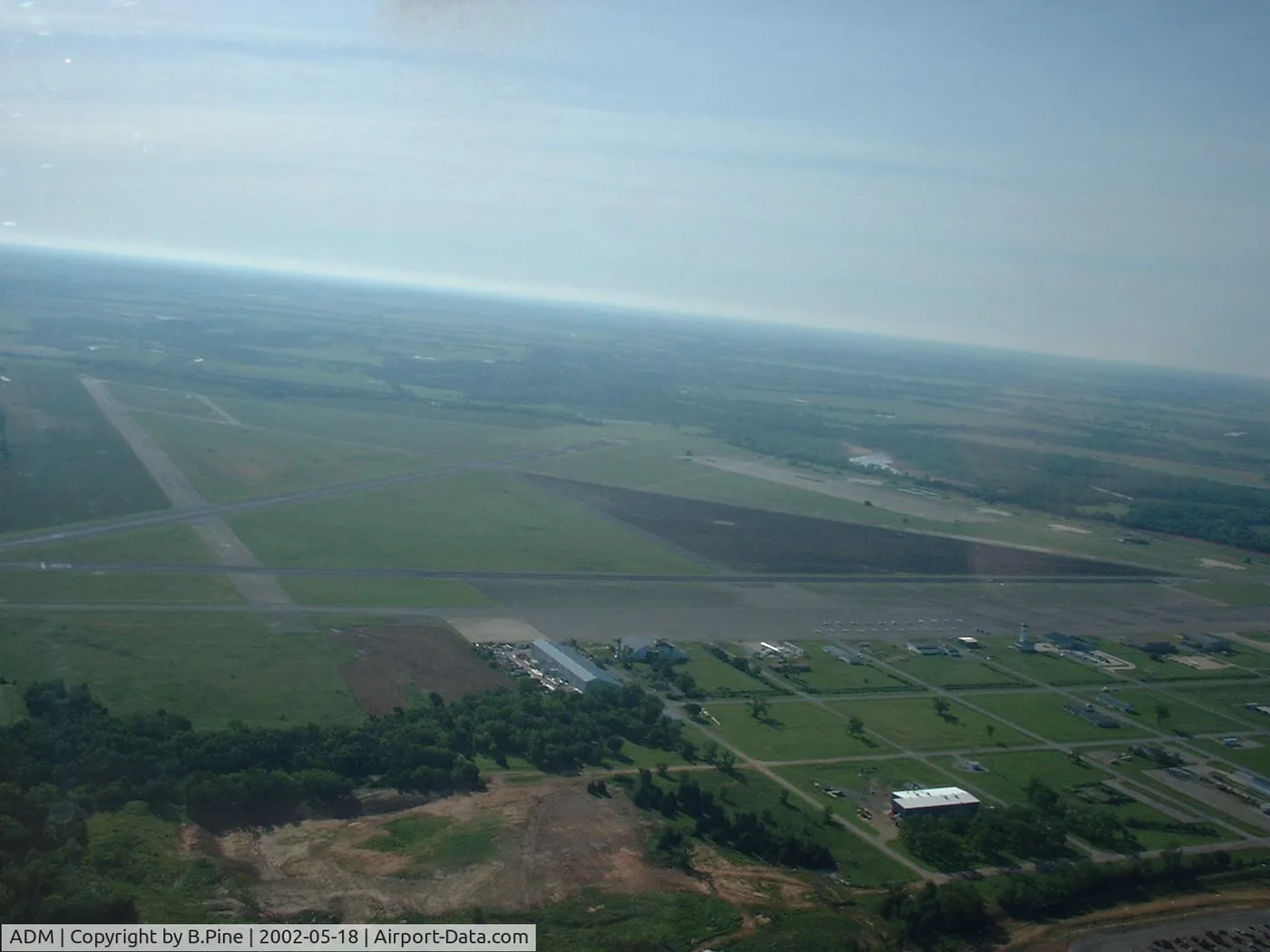 Luftaufnahme des Ardmore Municipal Airport – zwei Startbahnen kreuzen sich über grünen Feldern, Terminal und Hangars liegen geschlossen an der Südwestseite.