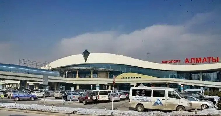 Ein Winterbild vor dem Terminal — Taxis und Kleinbusse im Schnee unter der diamantförmigen Dachspitze.