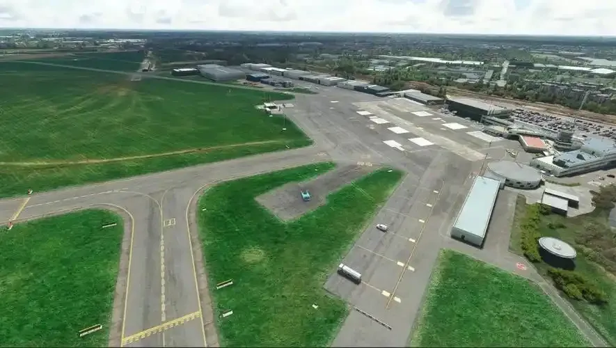 Antwerpen aus der Luft – Hangars verstreut zwischen der von Gras umgebenen Startbahn und den Rollwegen, rechts Straßen und Lagerhallen.