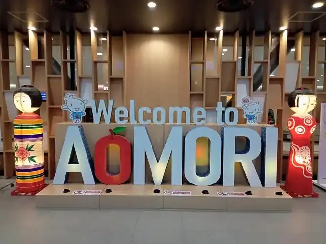 Im Terminal: „Welcome to AOMORI“ in Holzlettern neben zwei traditionellen Kokeshi-Puppen.
