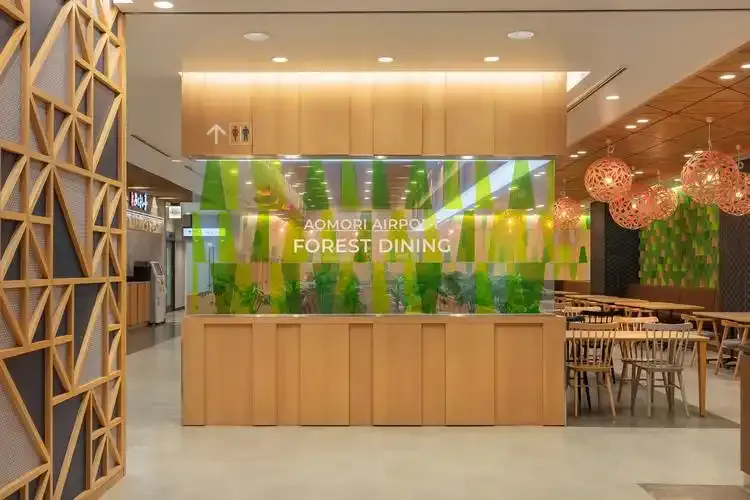 Der Food Court „AOMORI AIRPORT FOREST DINING“ – eine warme Holztheke vor einer begrünten Glaswand, rechts Tische.