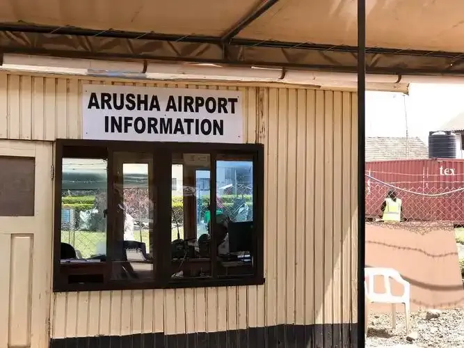 Der Informationsschalter „ARUSHA AIRPORT INFORMATION“ in seiner Holzhütte — die Einrichtungen des Flughafens auf einen Blick.